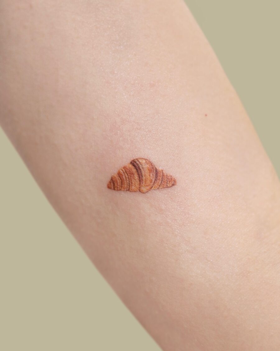 This croissant tattoo showcases stunning detail and rich colors, making it look almost edible.