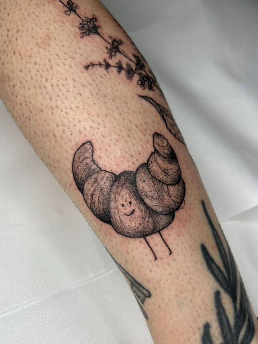 This cute croissant tattoo showcases a joyful character with a smiling face, adding a playful touch to body art.