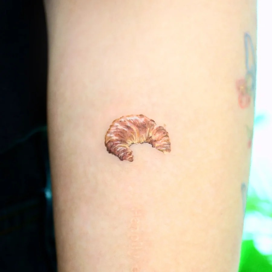 This tattoo features a beautifully detailed croissant, perfectly inked on the inner arm.
