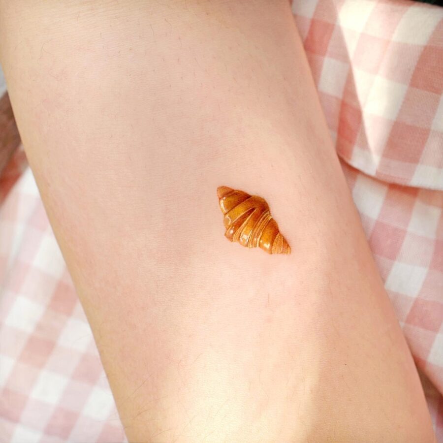This charming croissant tattoo exudes a delightful vibe with its warm, golden-brown hues.