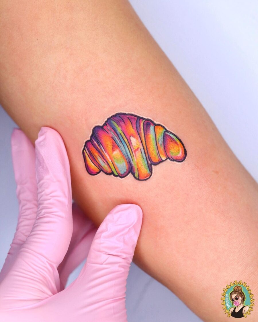 This croissant tattoo showcases a playful blend of colors that evoke a sense of joy.