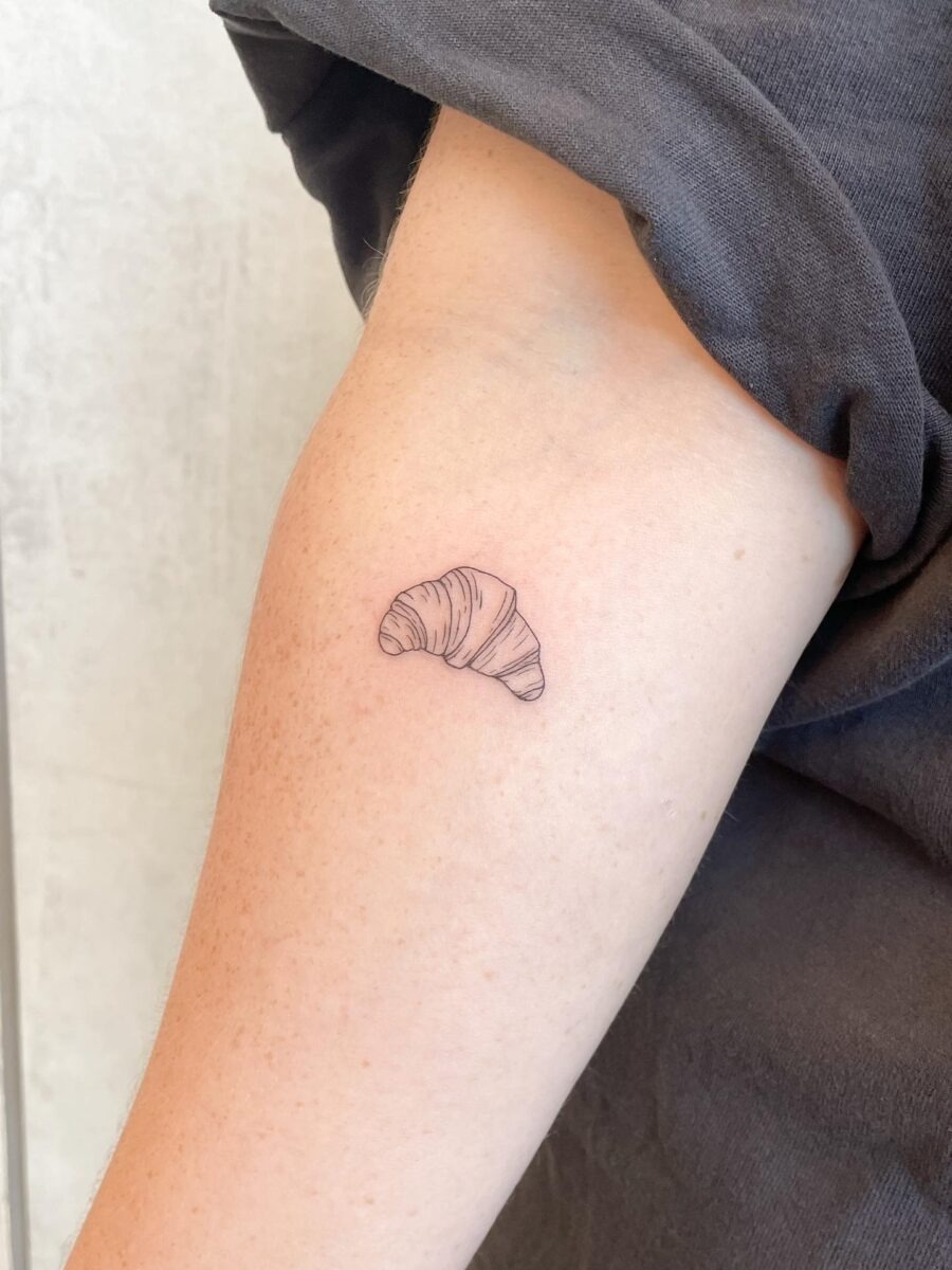 This minimalist croissant tattoo features subtle line work, exuding a chic and understated vibe.