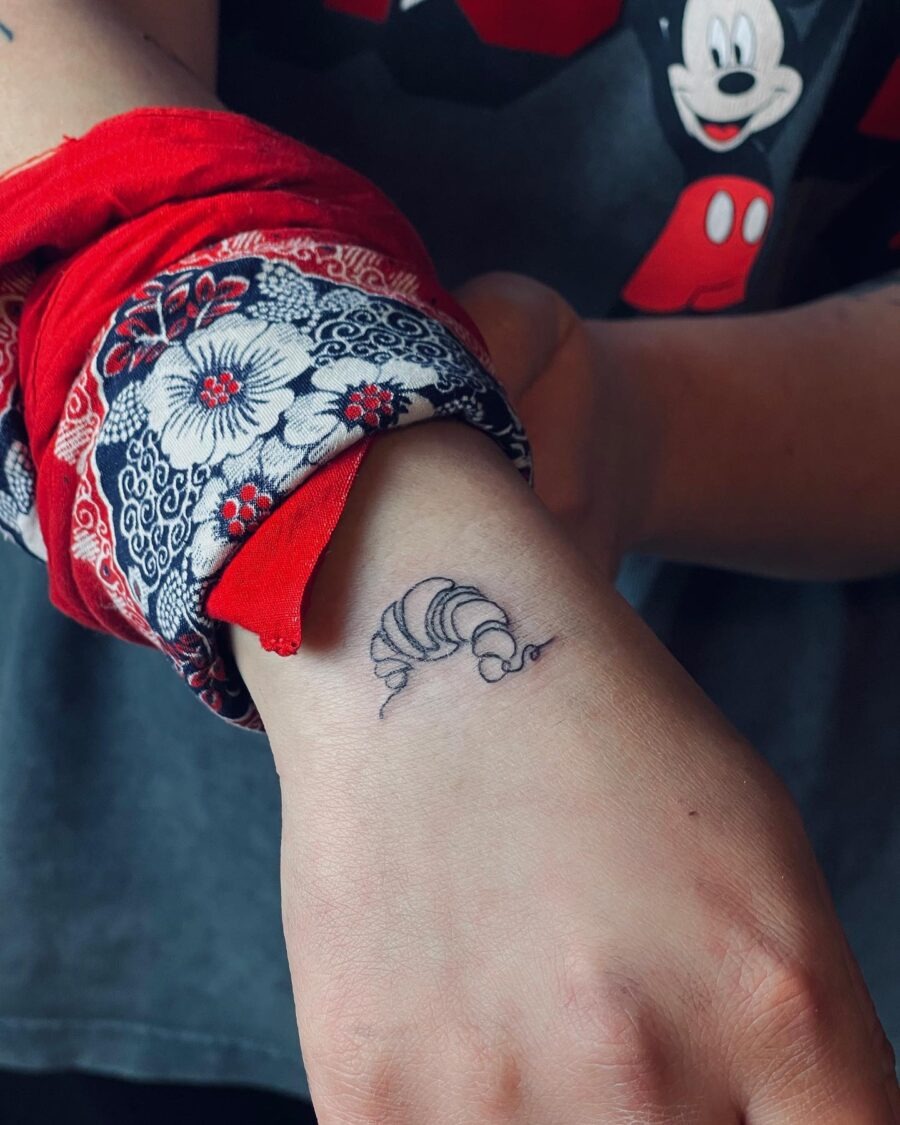 This charming tattoo features a minimalist croissant design inked on the wrist.