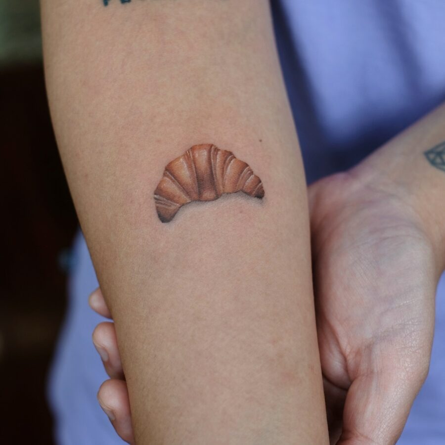 This tattoo features a beautifully realistic croissant, perfectly situated on the forearm.