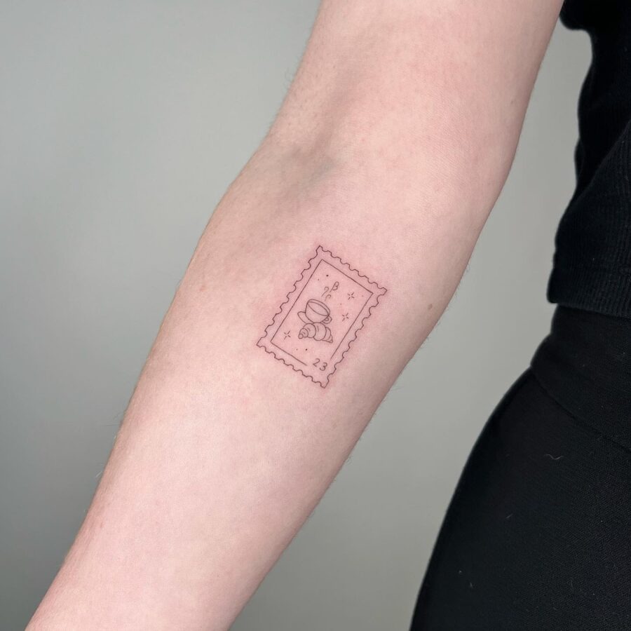 This tattoo features a dainty representation of a croissant inside the outline of a vintage postage stamp.