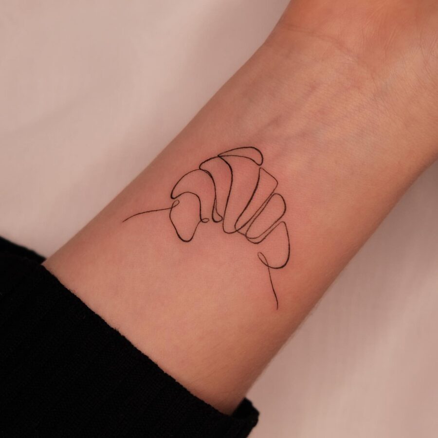 This croissant tattoo features a chic minimalist line art style.
