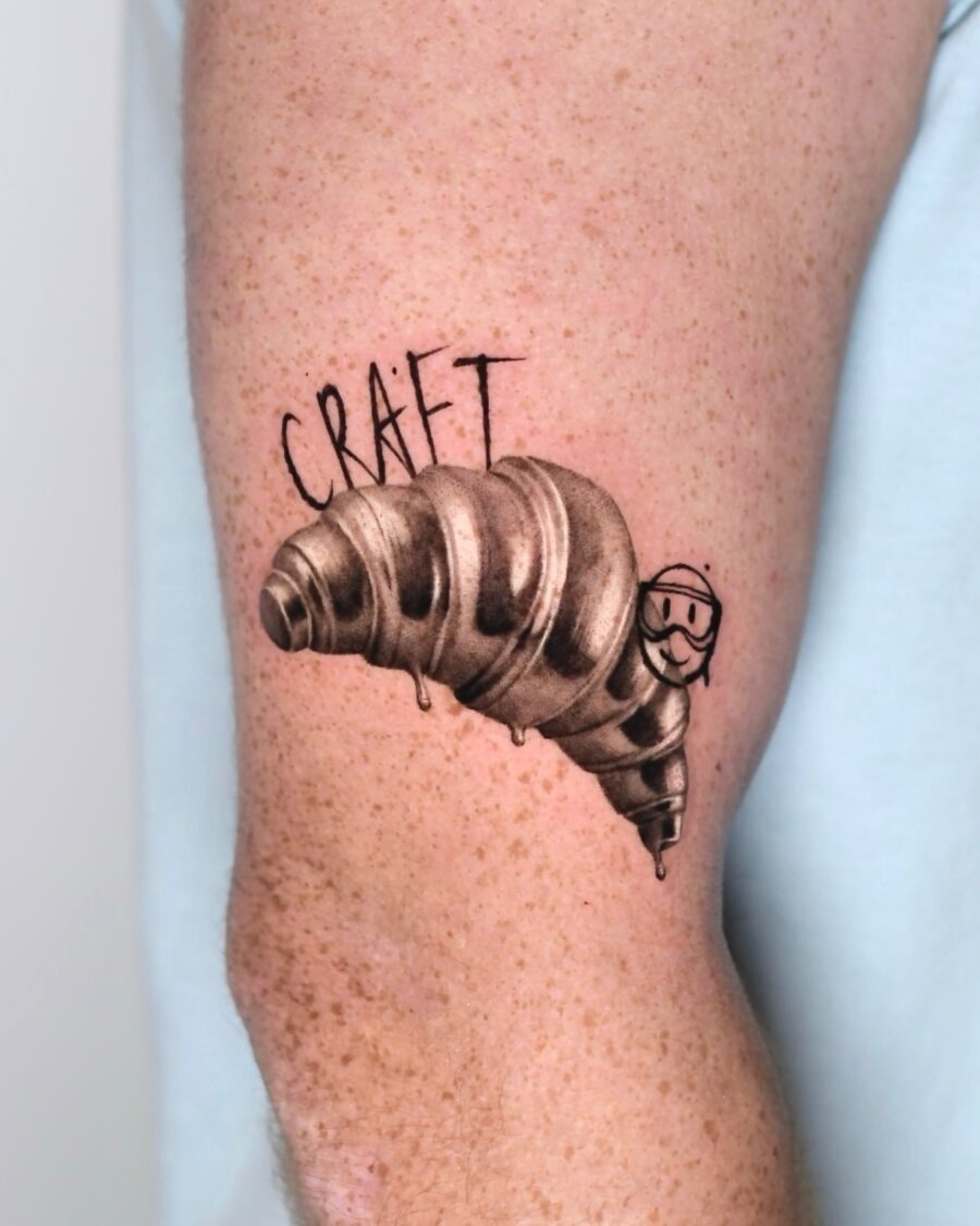This tattoo showcases a creatively designed croissant with a whimsical smiley face.