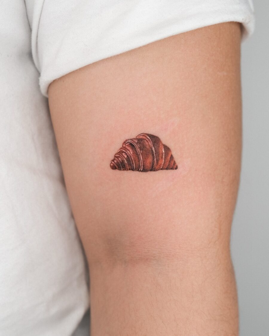 This tattoo showcases a beautifully detailed croissant on the inner arm.