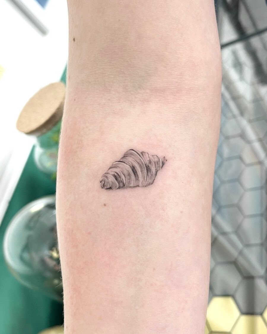 This tattoo presents a beautifully realistic depiction of a croissant, capturing its flaky texture and curve.