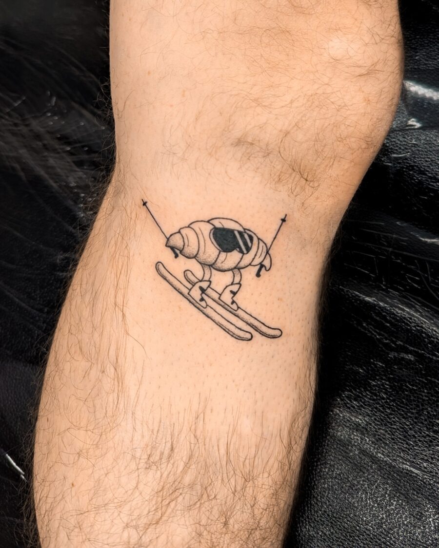 This playful tattoo features a croissant skiing down a slope, embodying a unique blend of humor and creativity.