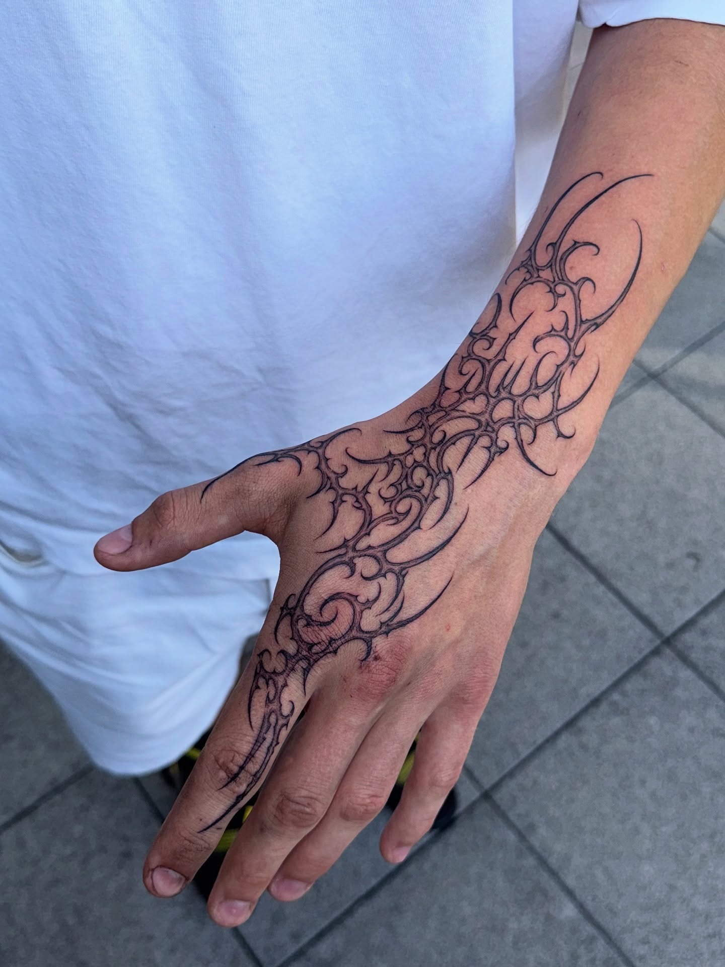 Intricate cybersigilism tattoo draped across woman's hand and fingers with needle fine tendrils