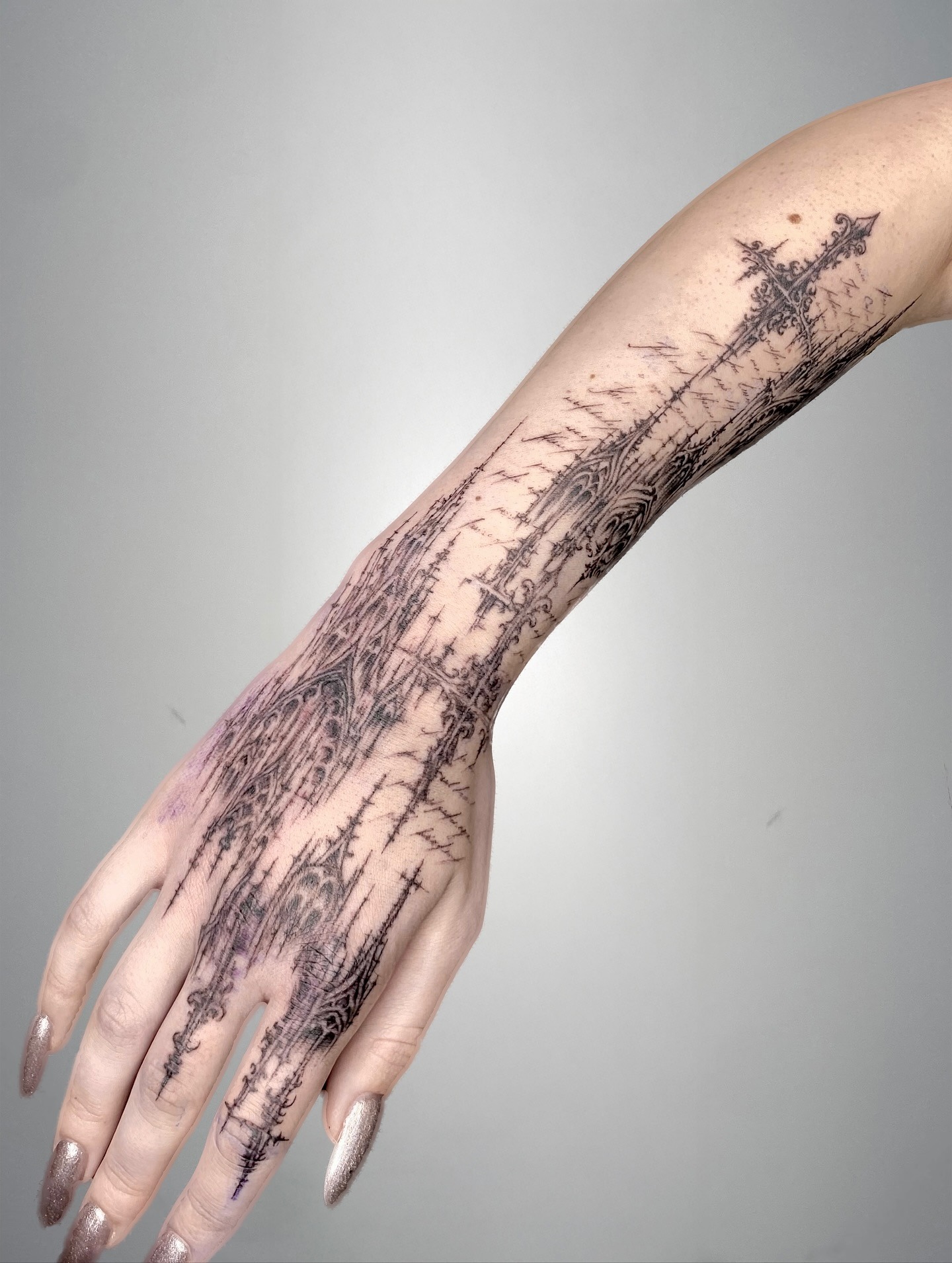 Cybersigilism gothic sword tattoo with pointed cathedral arches and sharp barbed tendrils on forearm