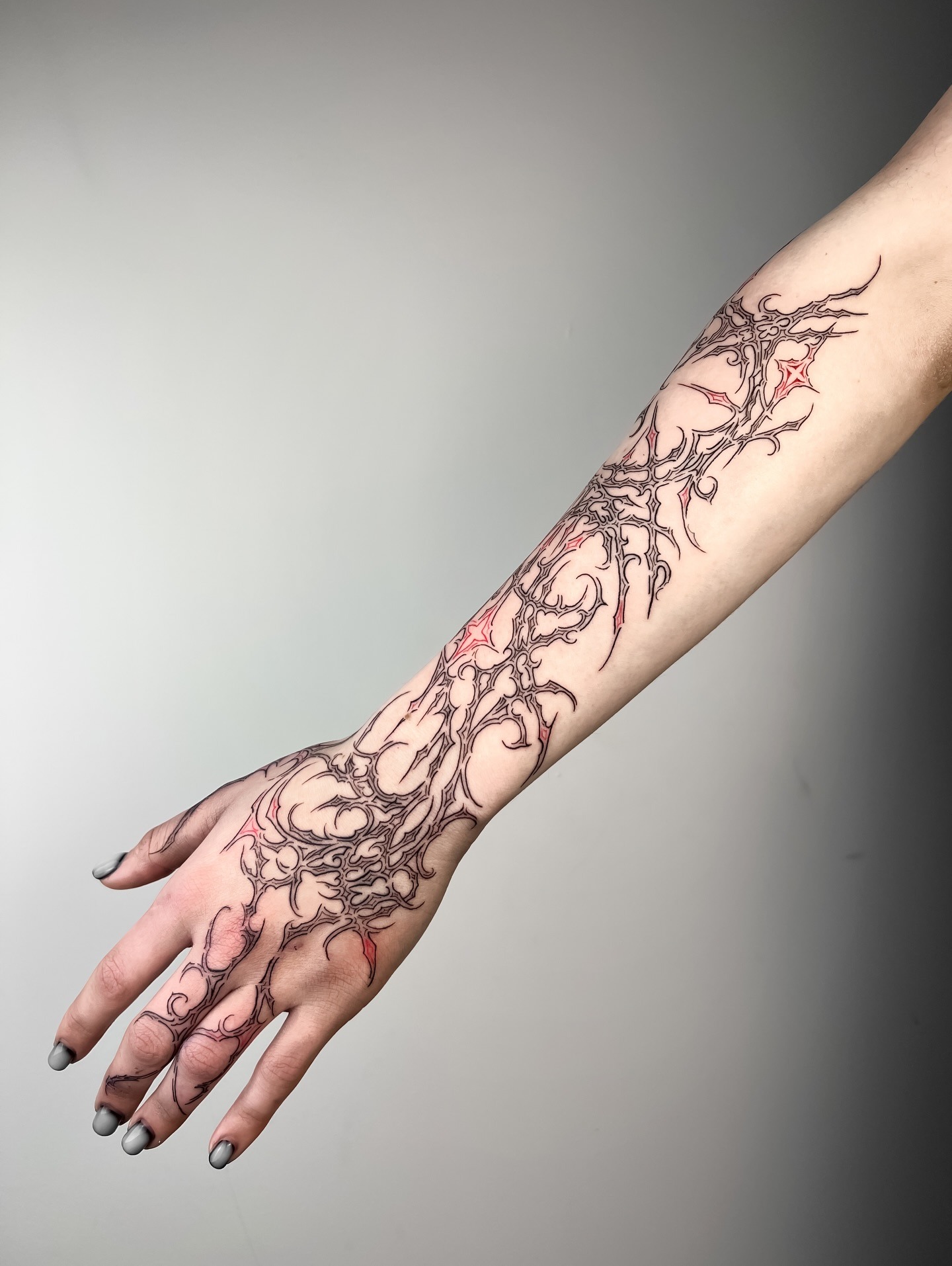 Black cybersigilism sleeve tattoo accented with vibrant red fluid bloodlines on forearm