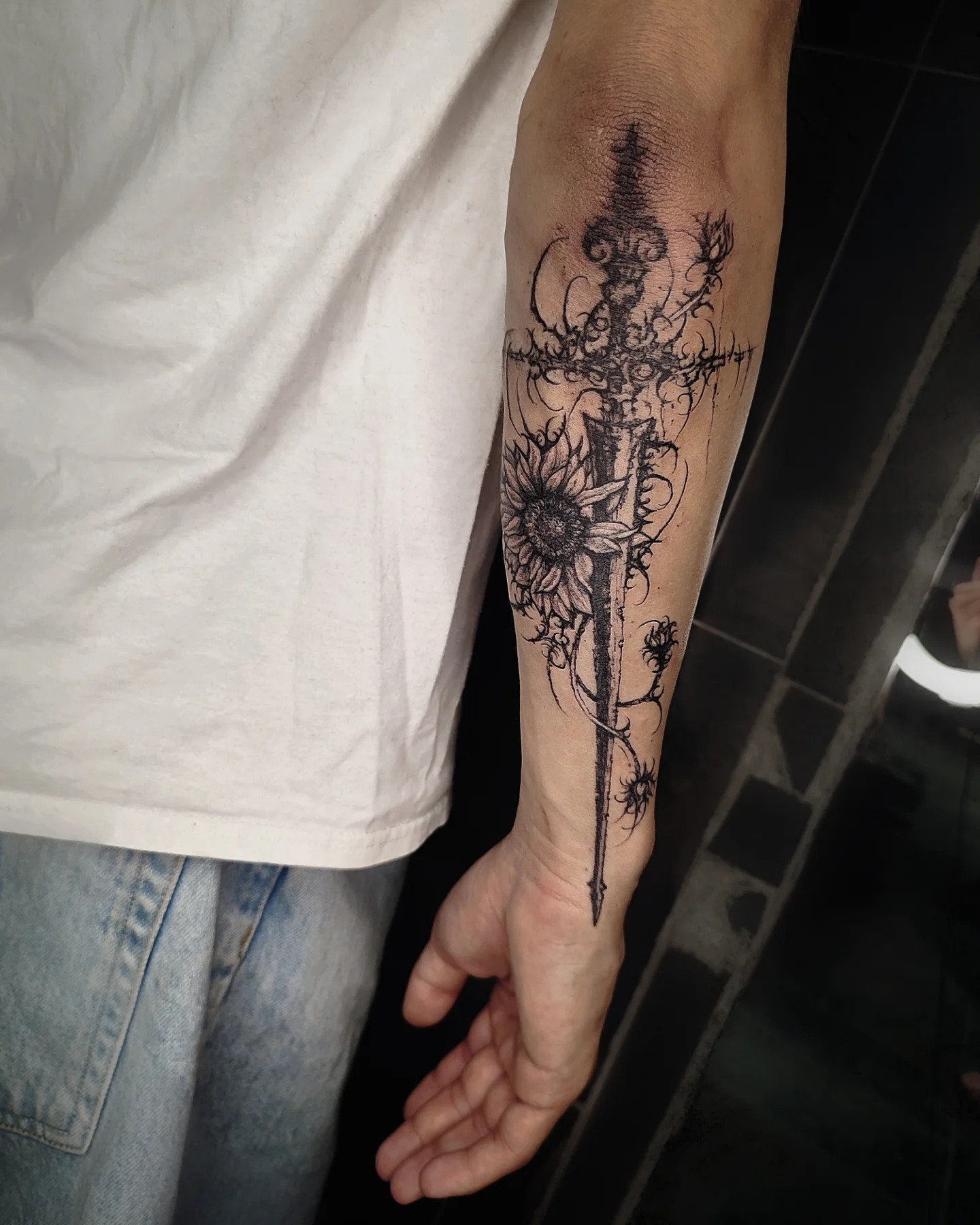 Gothic sword cybersigilism tattoo piercing through a blooming sunflower on arm