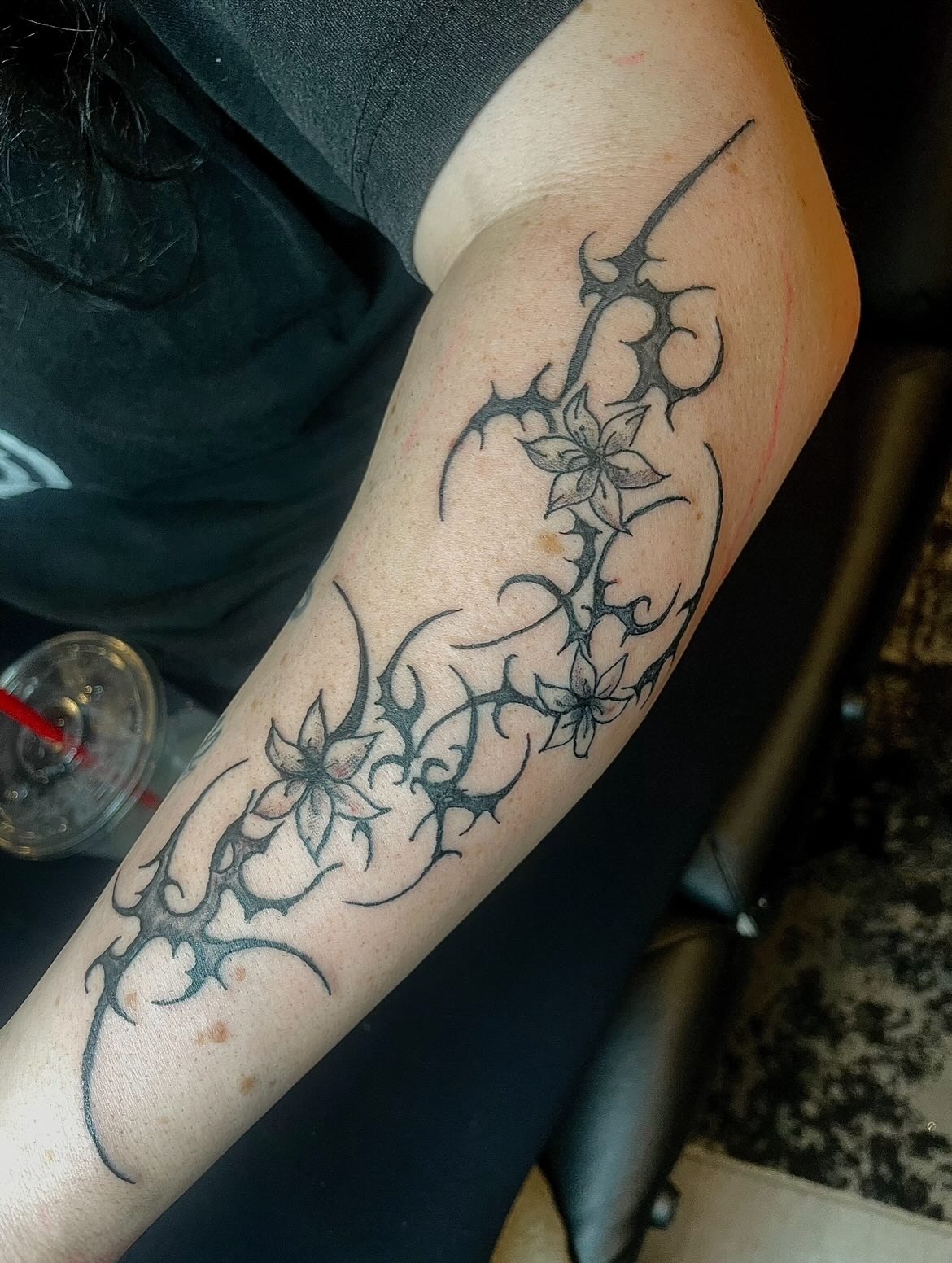 Blackwork thorn vine tattoo wrapping around a delicate opening blossom with cyber accents
