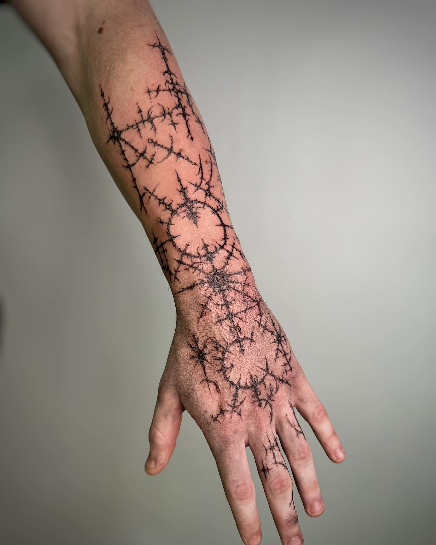 Angular cybersigilism spider web tattoo on elbow with sharp geometric strands