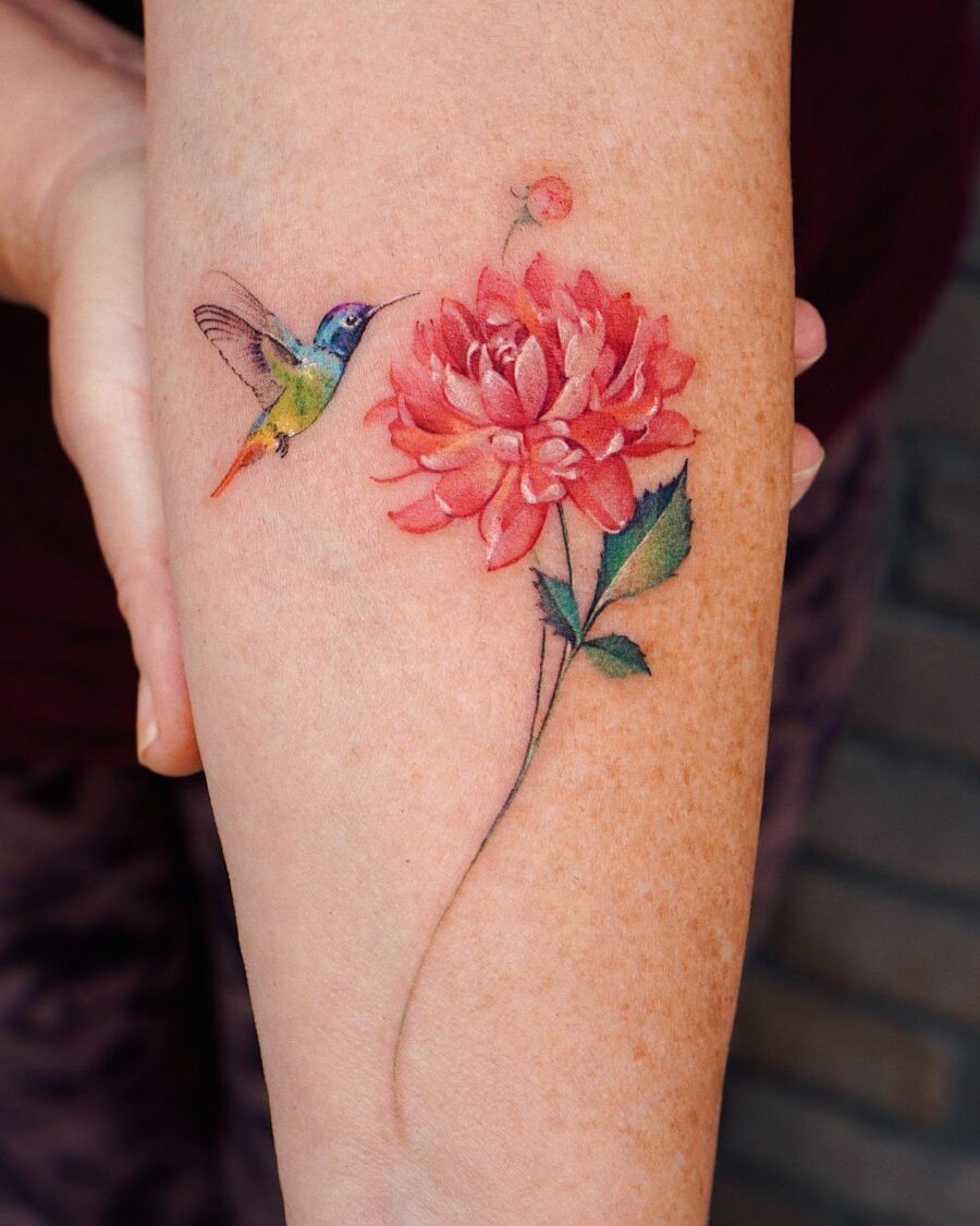 This tattoo features a stunning dahlia in bloom, paired with a delicate hummingbird hovering nearby.