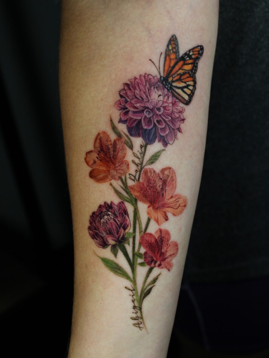 This dahlia tattoo features a stunning blend of vivid flowers and a delicate butterfly perched on top.