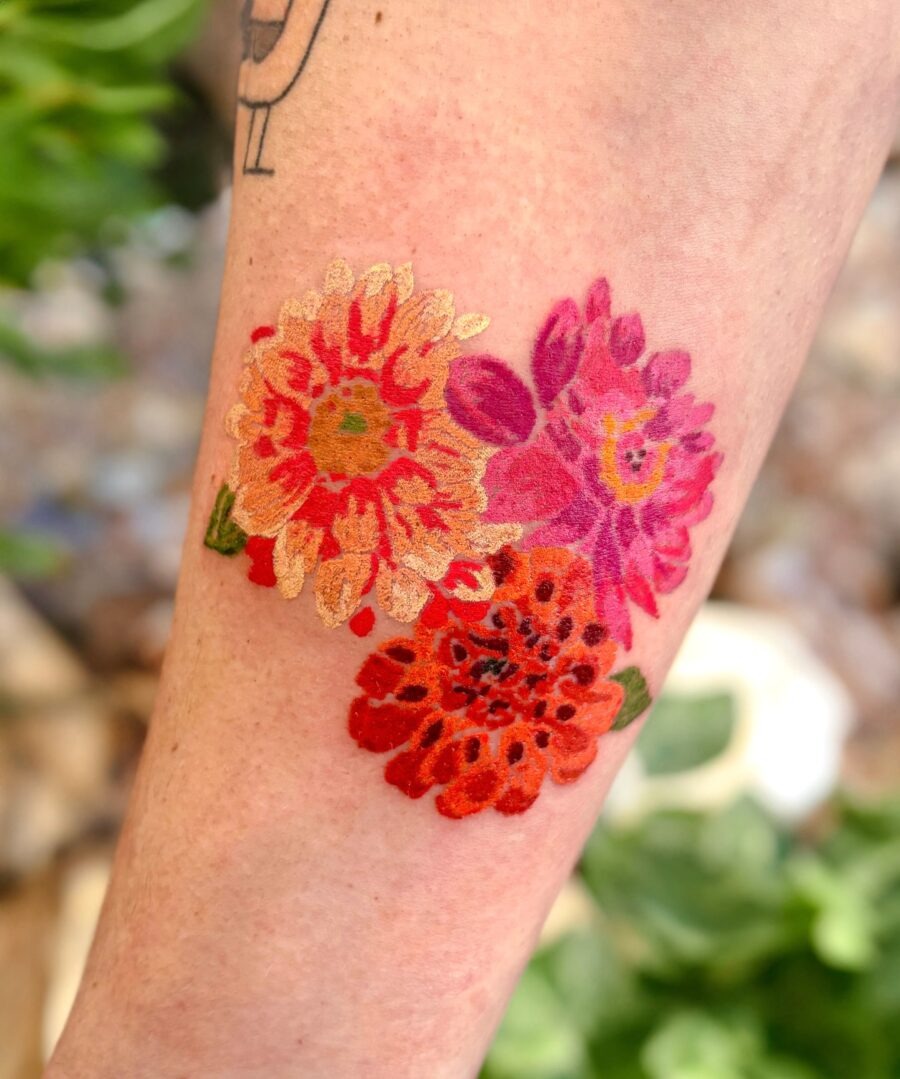 This dahlia tattoo showcases bold colors in red, pink, and orange, capturing the essence of summer blooms.
