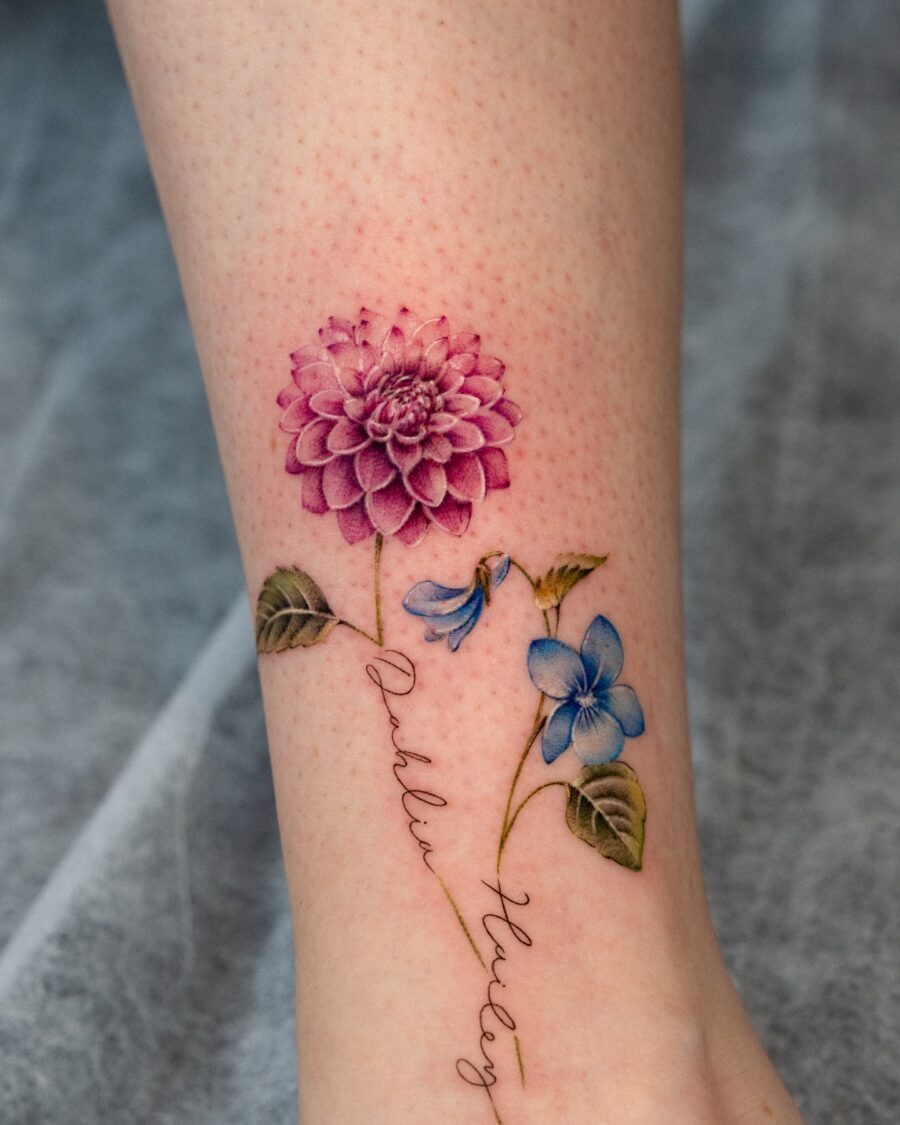 This tattoo showcases a stunning dahlia in pink, accompanied by delicate blue flowers.