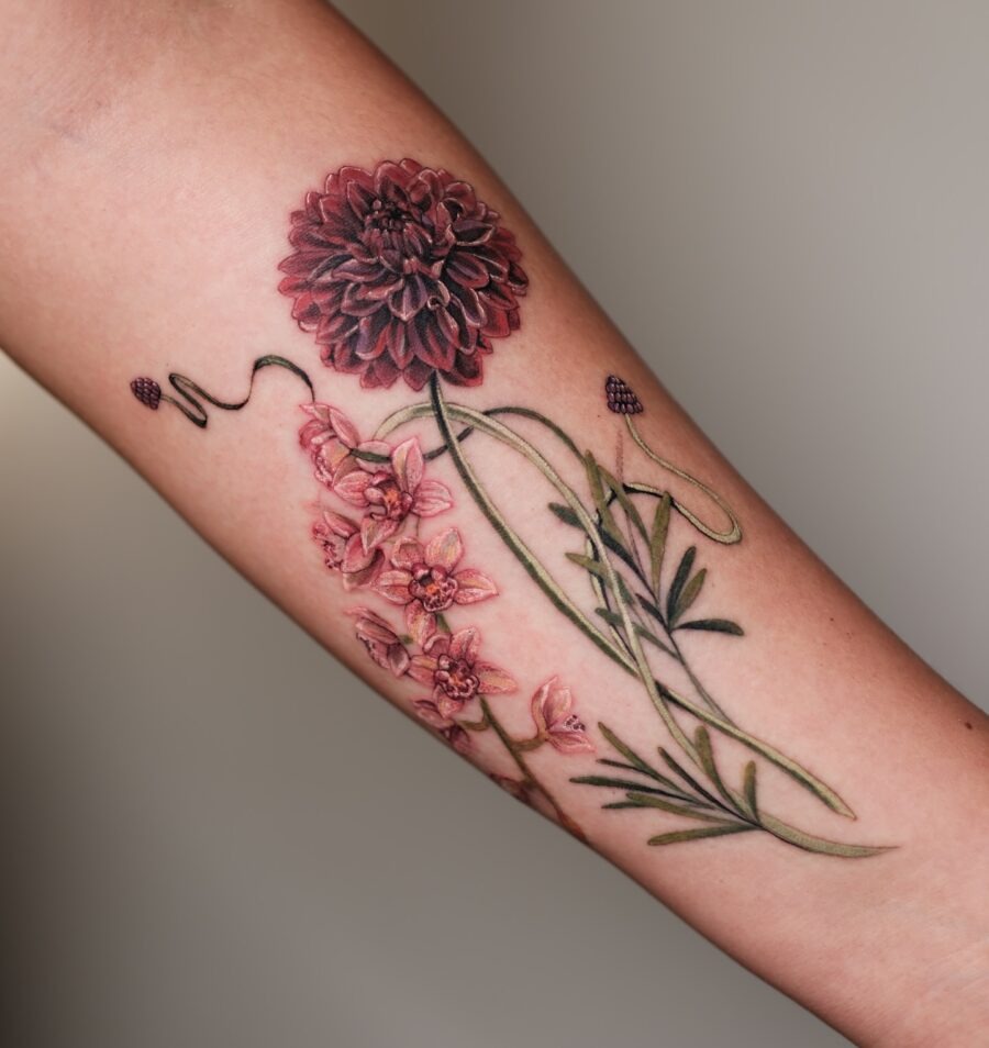 This tattoo captures a stunning dahlia in deep burgundy, surrounded by delicate pink blossoms and green foliage.