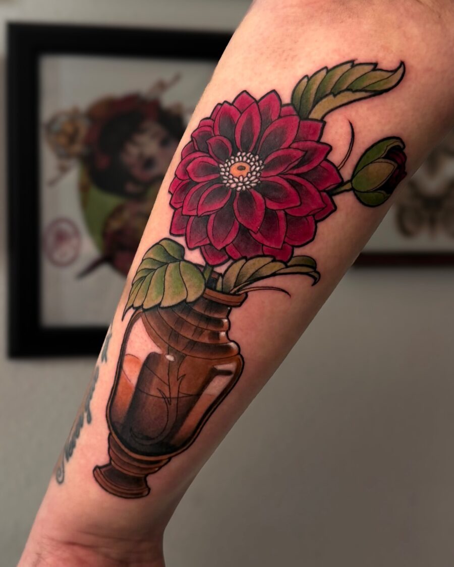 This stunning dahlia tattoo features a pink flower elegantly paired with a traditional vase.