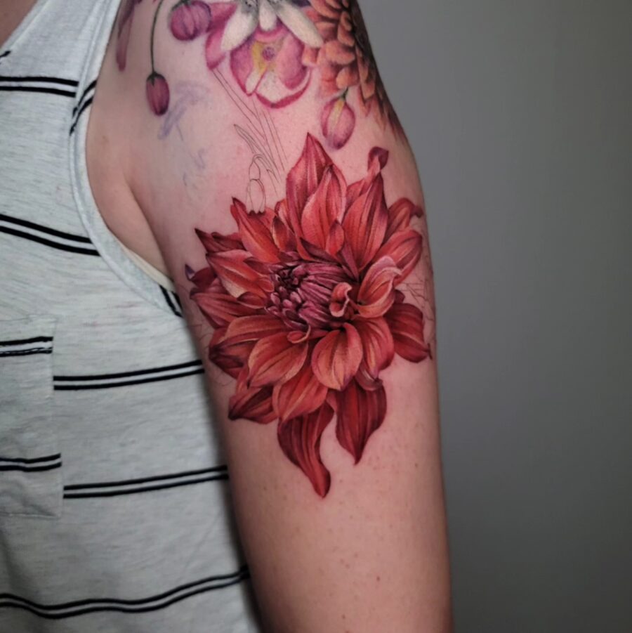 This striking dahlia tattoo on the arm features deep red petals and intricate detailing, giving it a lifelike appearance.