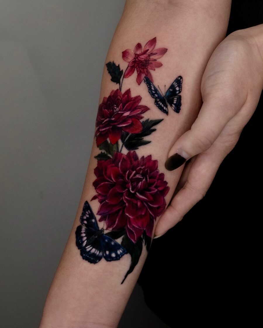 This tattoo features dahlias in rich shades of red, adorned with delicate butterflies.