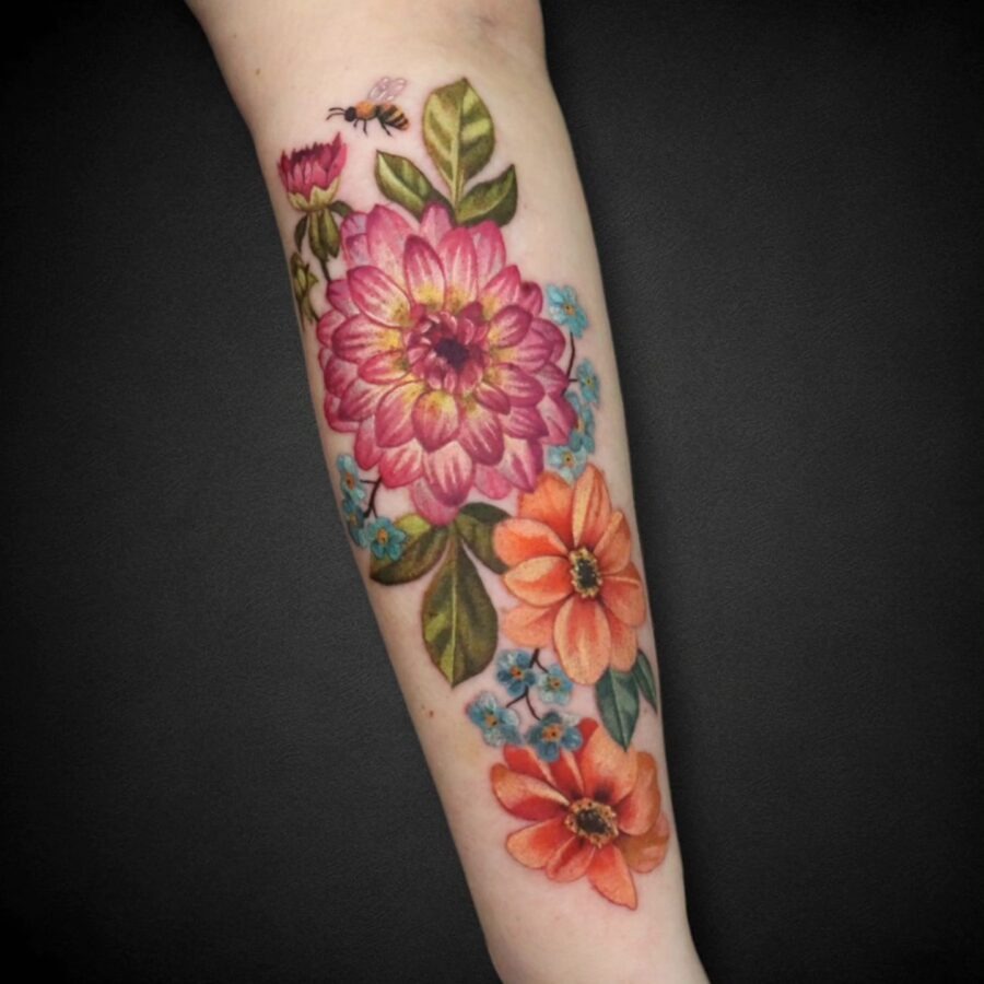 This vivid dahlia tattoo showcases intricate pink and orange blooms, intertwined with greenery.
