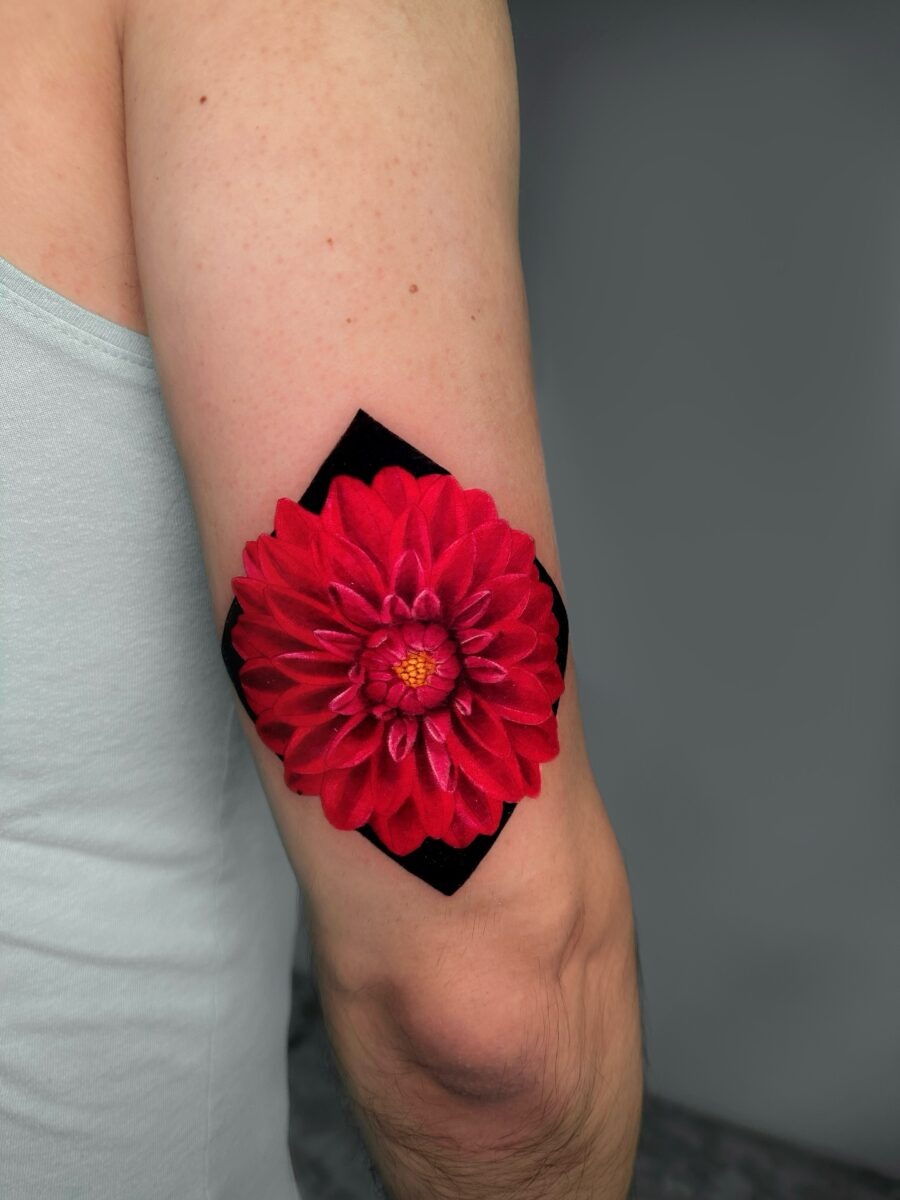 This stunning dahlia tattoo features a bold red flower accentuated by a dark geometric background.