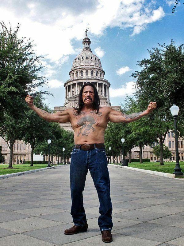 Trejo stands with arms raised before a grand capitol building, his chest tattoo fully displayed.