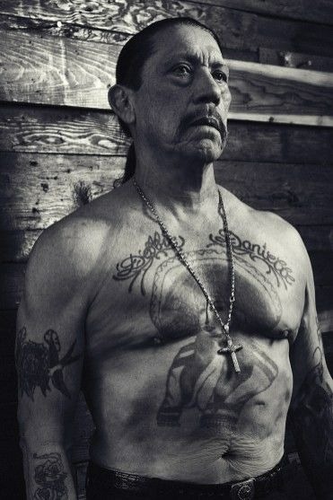 Trejo's arms rest on his shoulders as he sits against a backdrop of lush red roses.