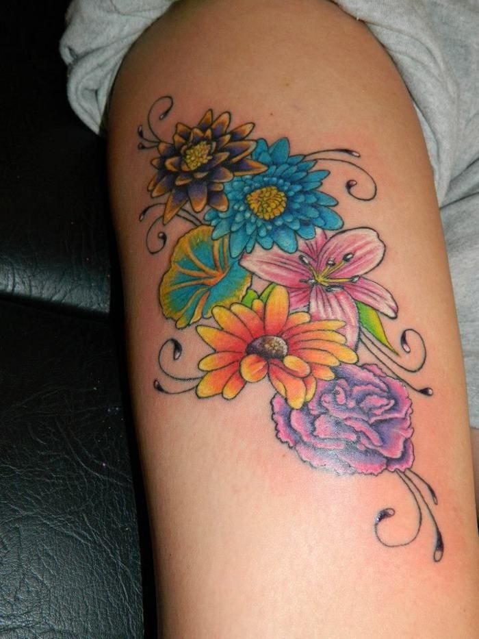 This colorful tattoo features a mix of flowers, including bold blue and pink blooms with intricate petal detailing.