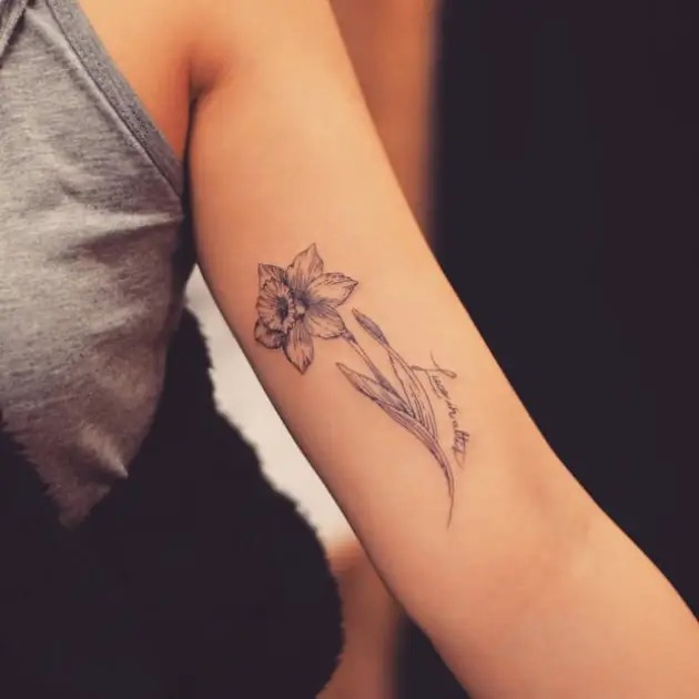 This tattoo emphasizes simplicity with a single Narcissus flower and slender leaves sketched with clean, fine lines.