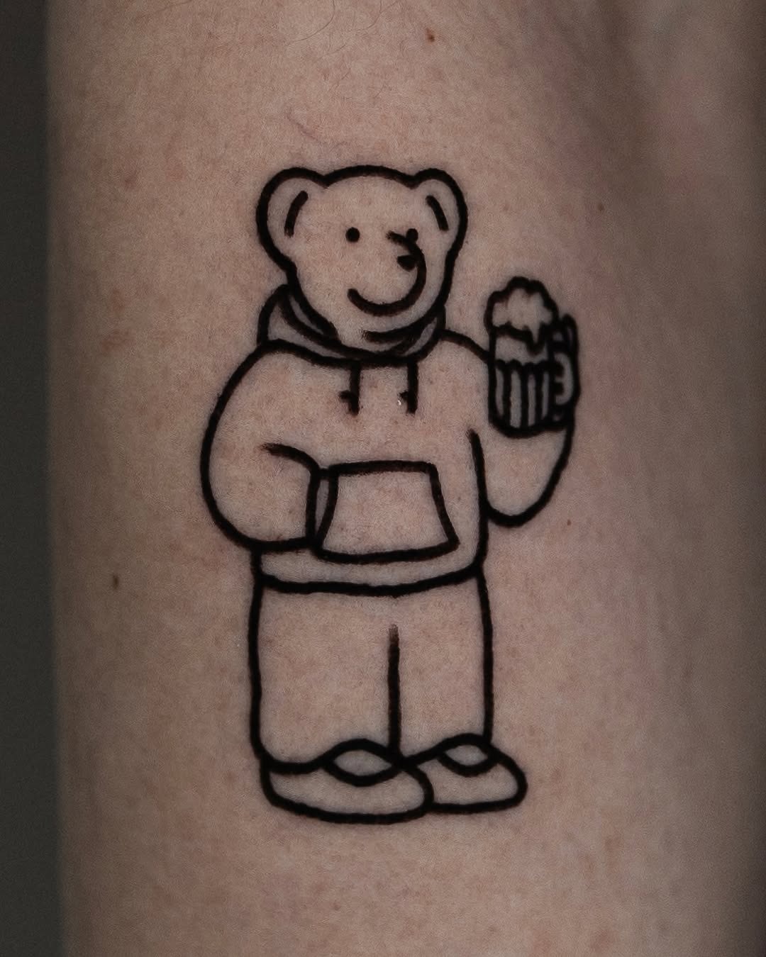 This cute bear tattoo features an inviting cartoon design, complete with a hoodie and a beer mug.