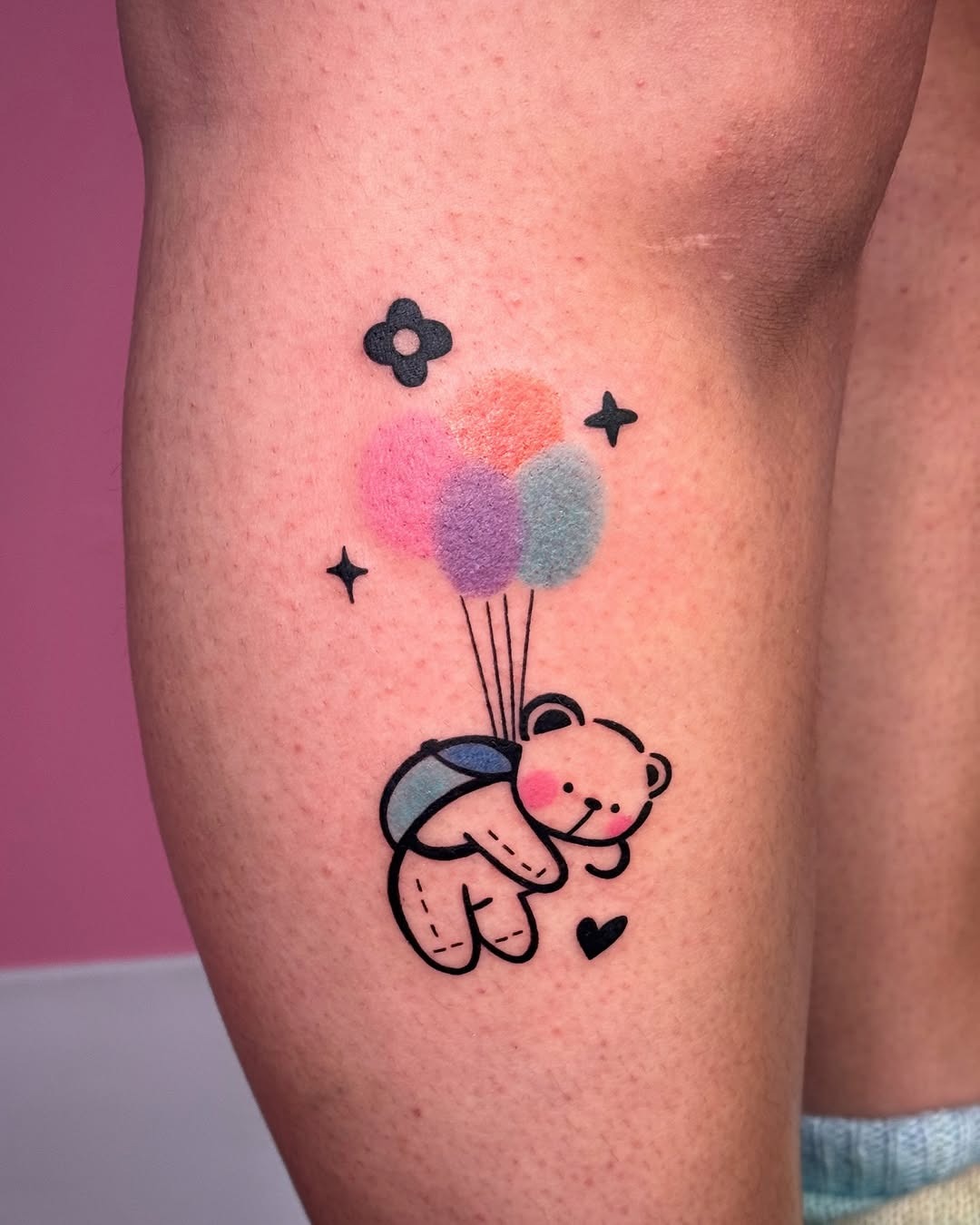 This charming tattoo features a cute bear holding colorful balloons, radiating a sense of joy and whimsy.