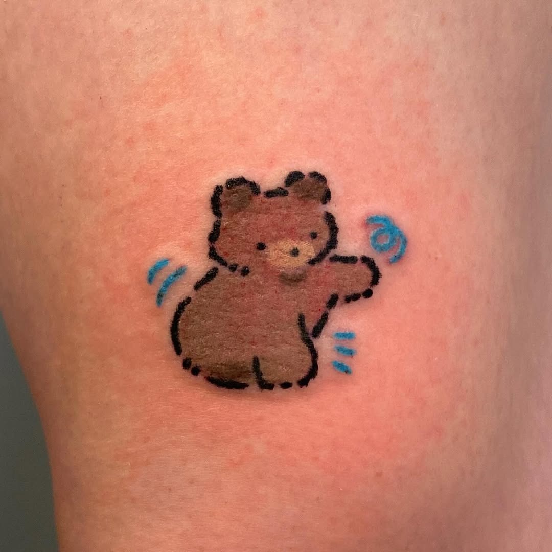 This tattoo showcases a cute, cartoonish bear sitting with a cheerful expression.