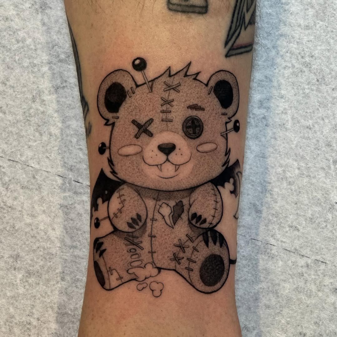 This tattoo showcases a charming bear with stitched patterns, embodying a playful yet edgy aesthetic.