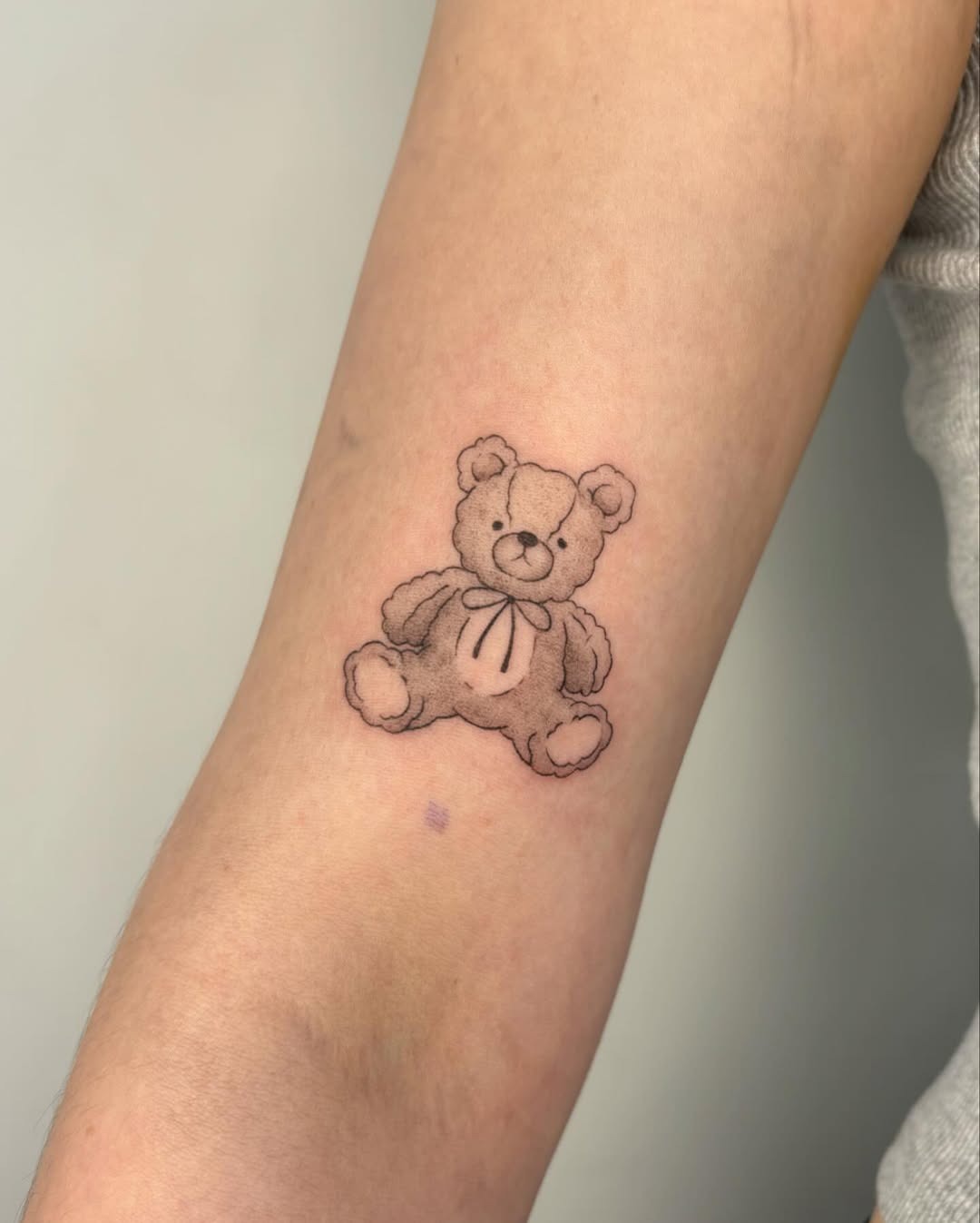 This tattoo showcases a playful teddy bear with a soft, inviting expression.