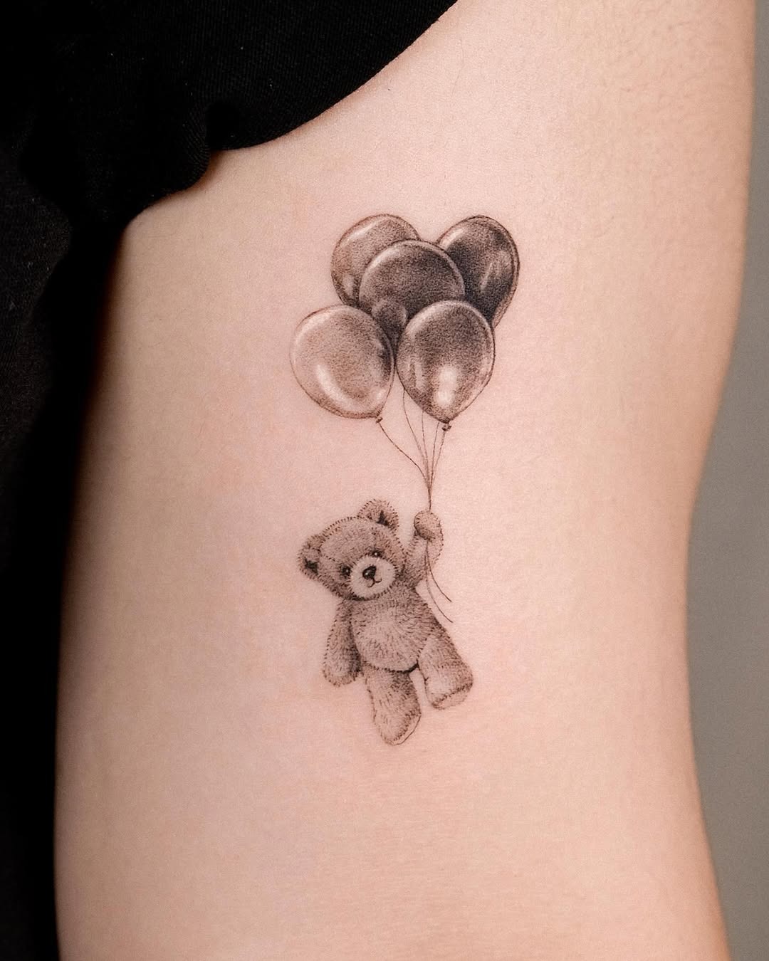 This tattoo features an adorable stuffed bear holding onto colorful balloons.