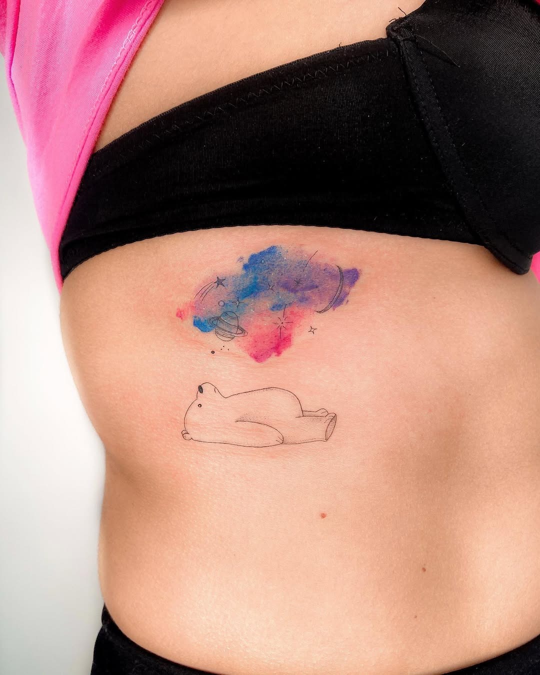 This playful tattoo features a dreamlike bear lying peacefully, surrounded by watercolor splashes.