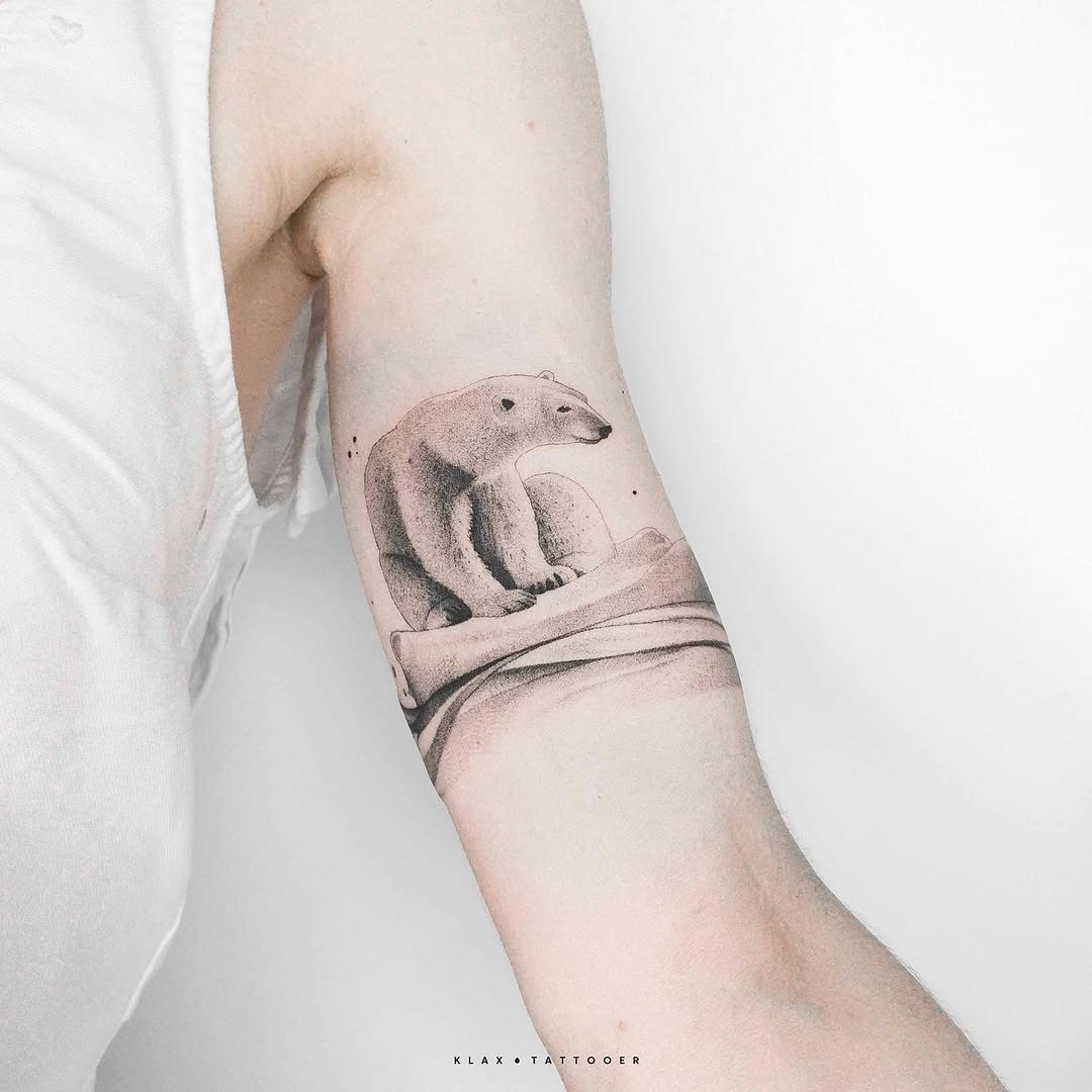 This tattoo features a beautifully minimalist polar bear resting on a smooth surface.