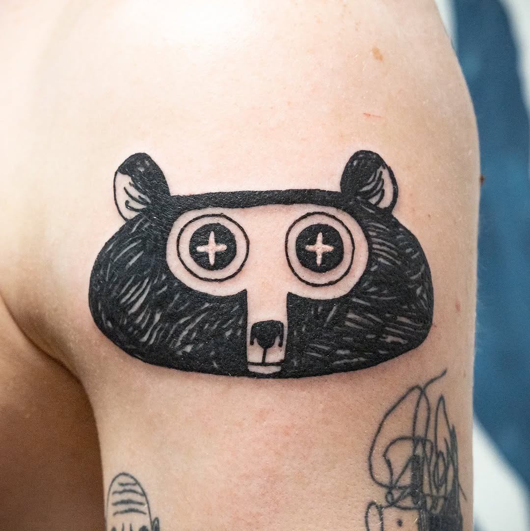 This tattoo showcases a stylized bear head with large, playful eyes and a minimalistic design.