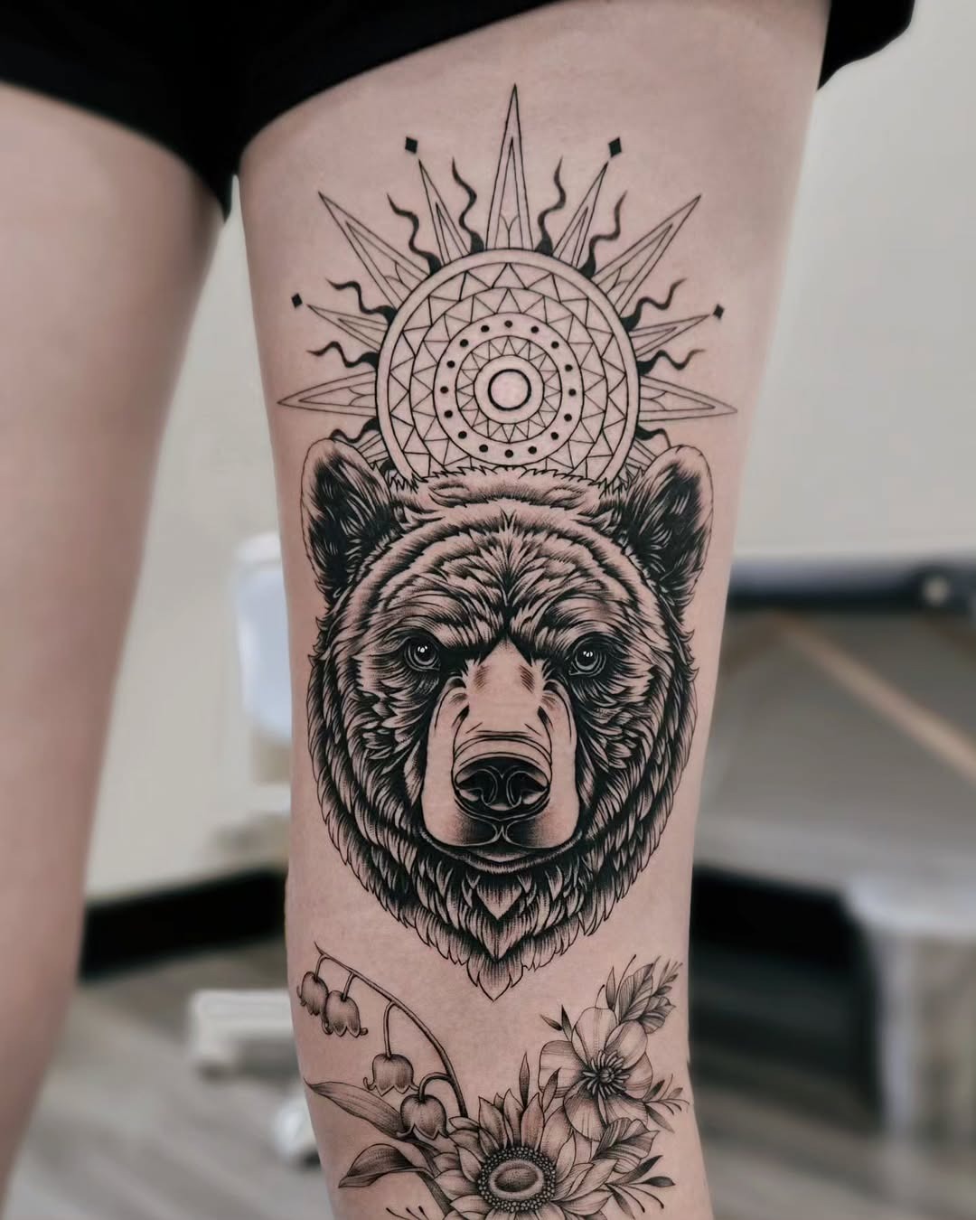 This striking bear tattoo features a detailed bear head, crowned by a radiant mandala sun.