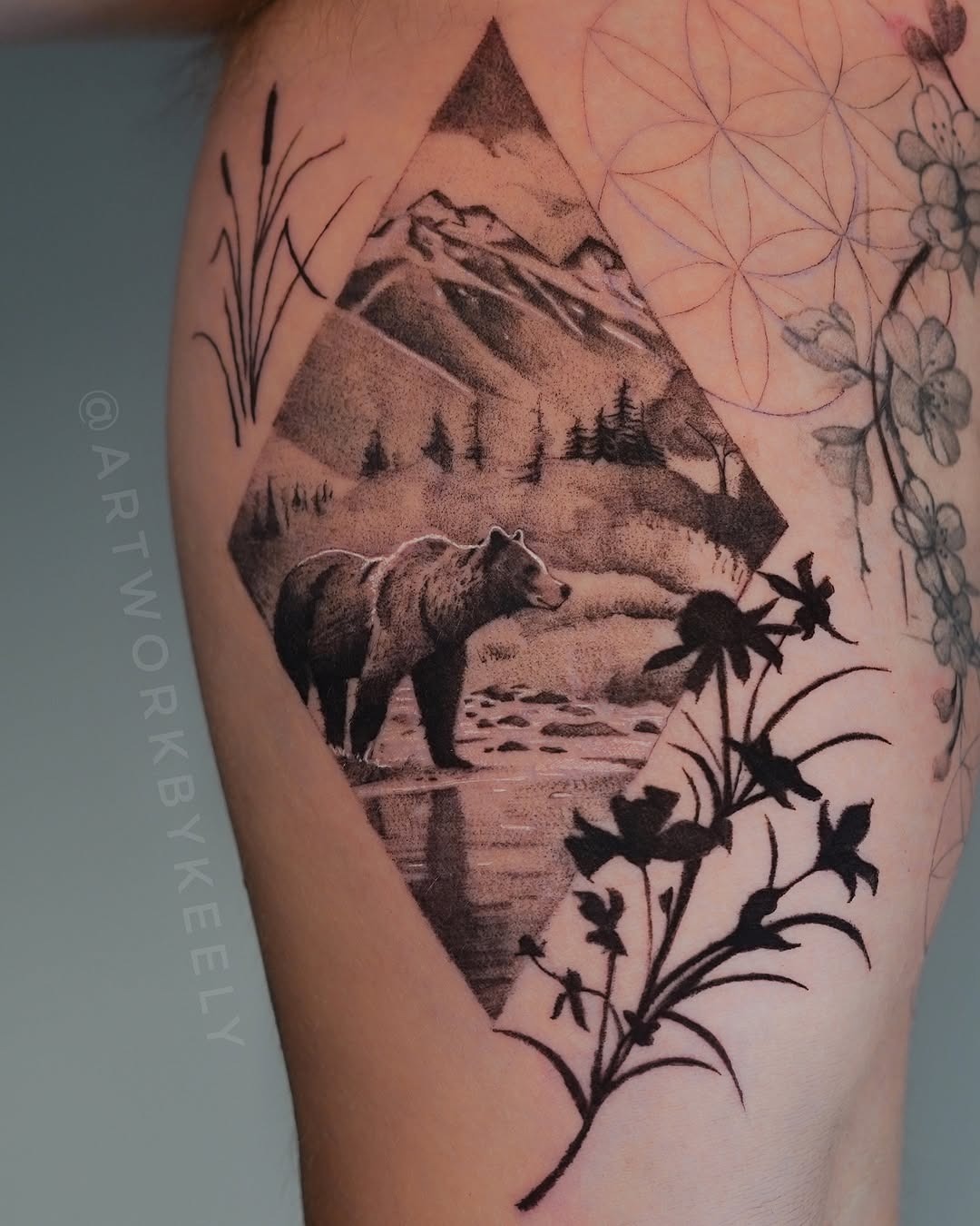 This intricate tattoo beautifully captures a bear against a serene landscape, framed in a diamond shape.