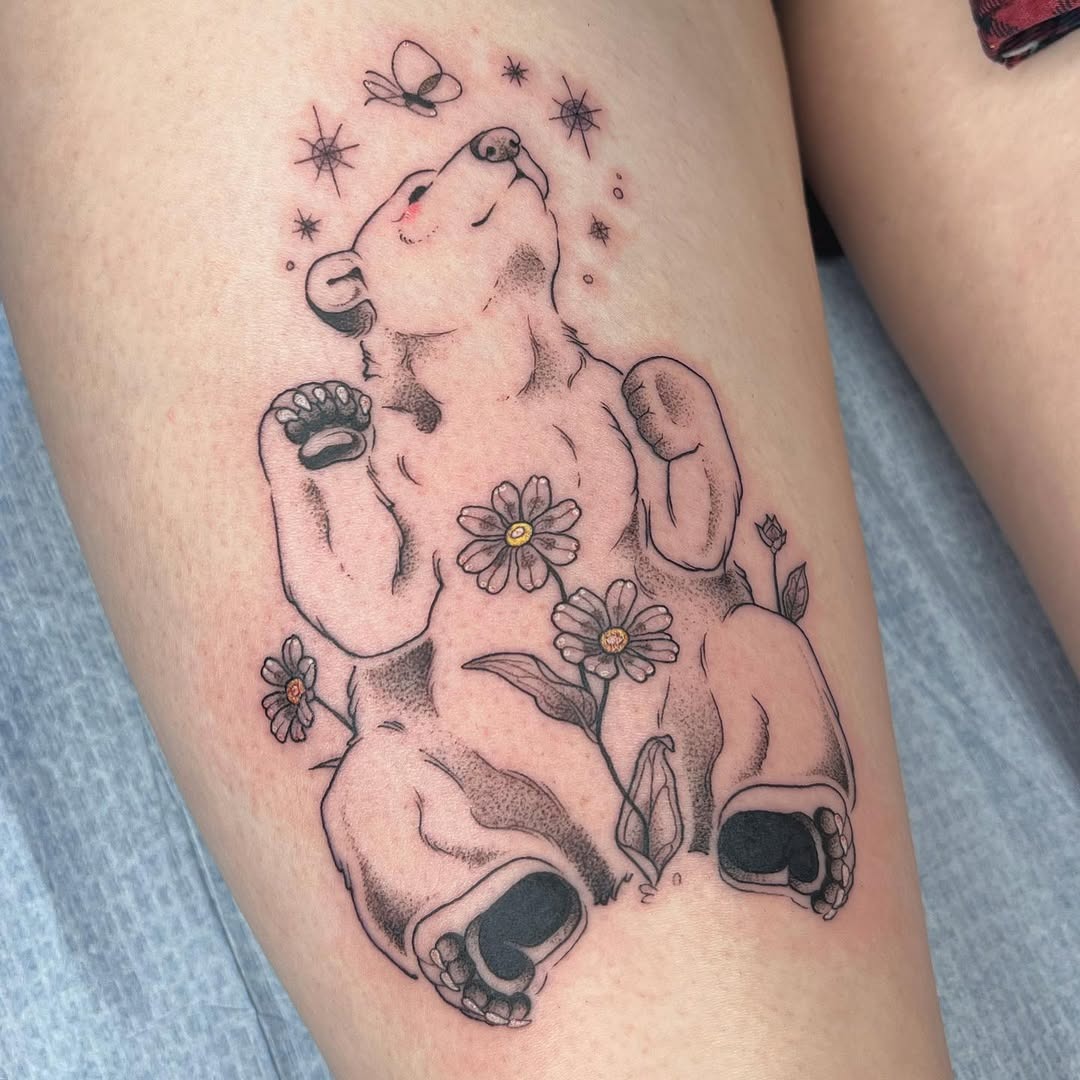 This bear tattoo exudes a playful and serene vibe, showing a reclining bear adorned with flowers and soft stars.