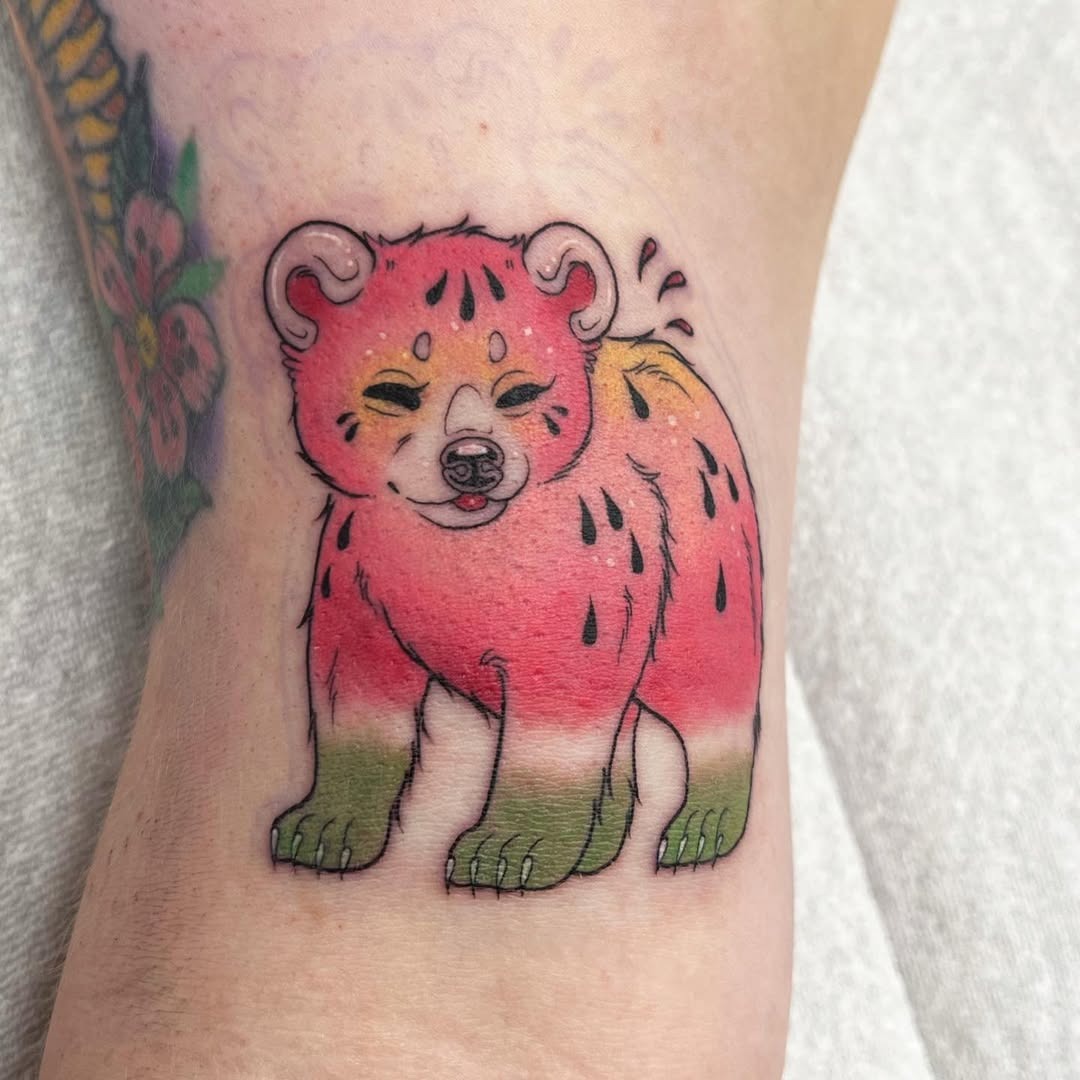 This tattoo features a cute bear designed with watermelon elements, blending playful colors in shades.