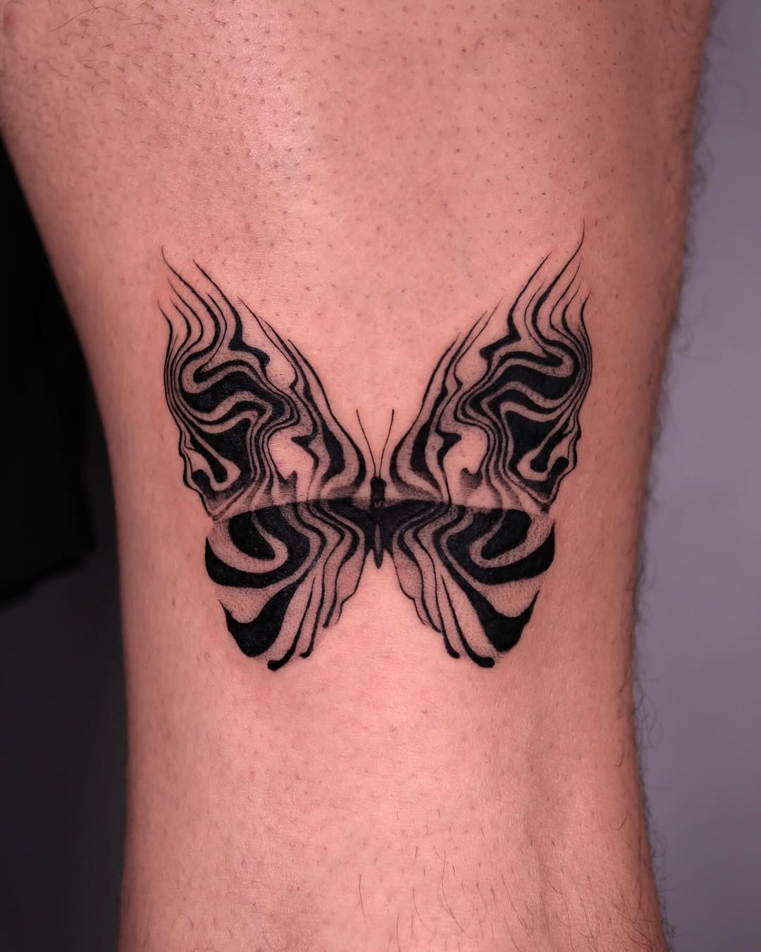 This tattoo features a striking butterfly design with abstract black ink patterns.