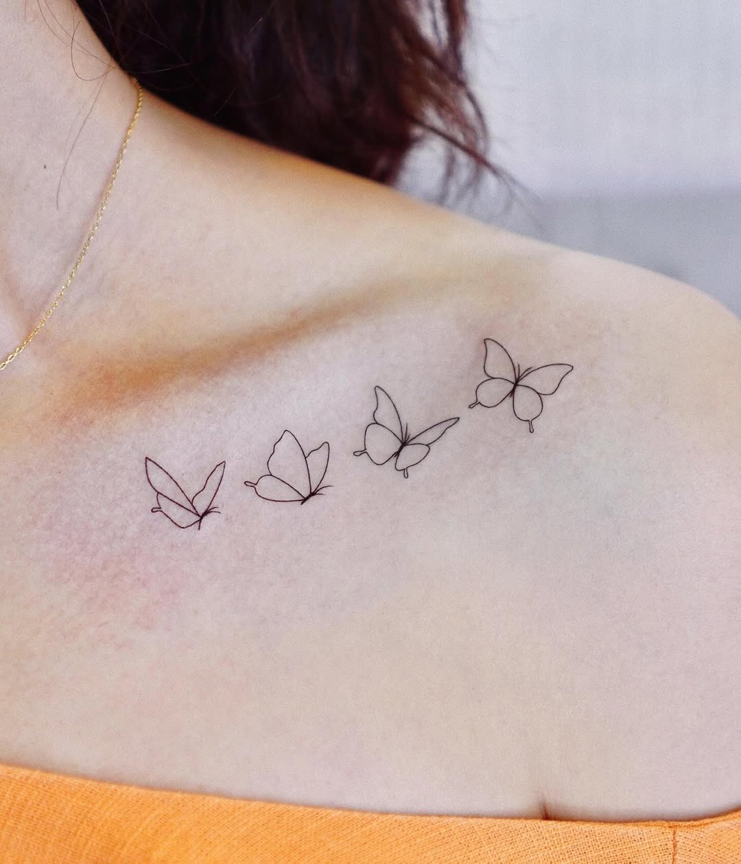 This tattoo features a series of delicate, minimalist butterflies inked on the shoulder.