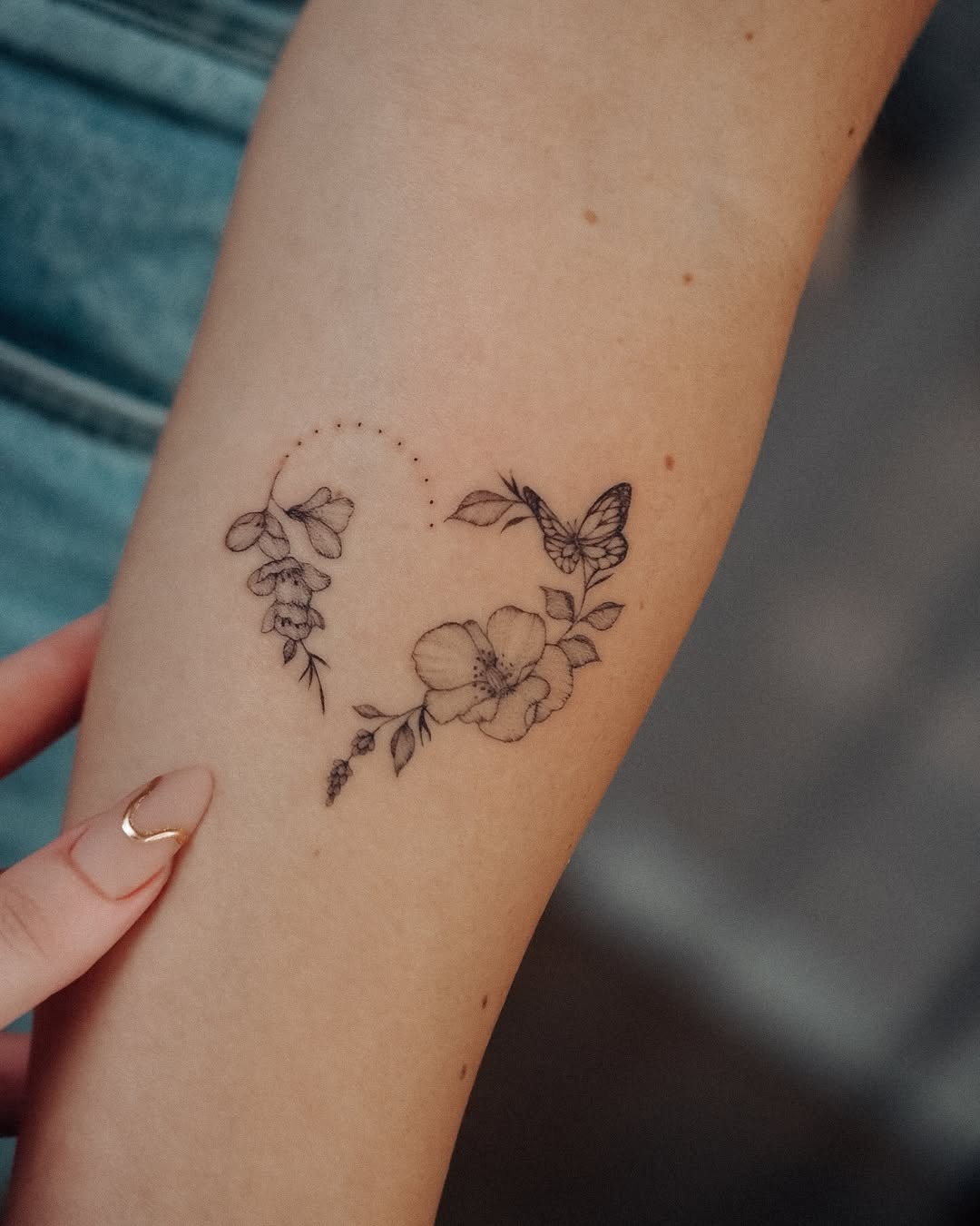 This beautiful tattoo showcases a butterfly surrounded by intricate flowers, forming a heart shape.